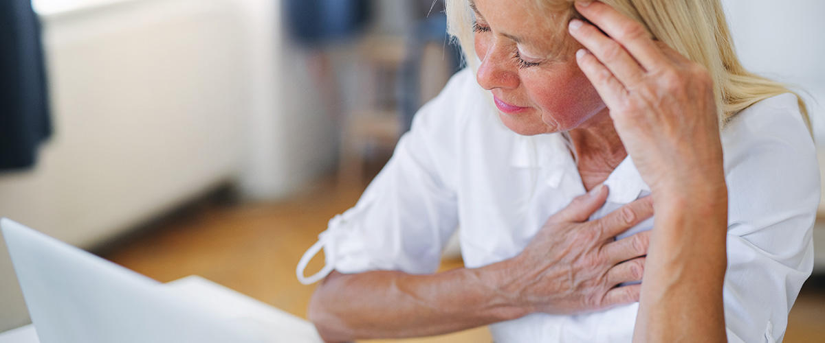 A woman in pain, with one hand on her chest and another hand on her forehead