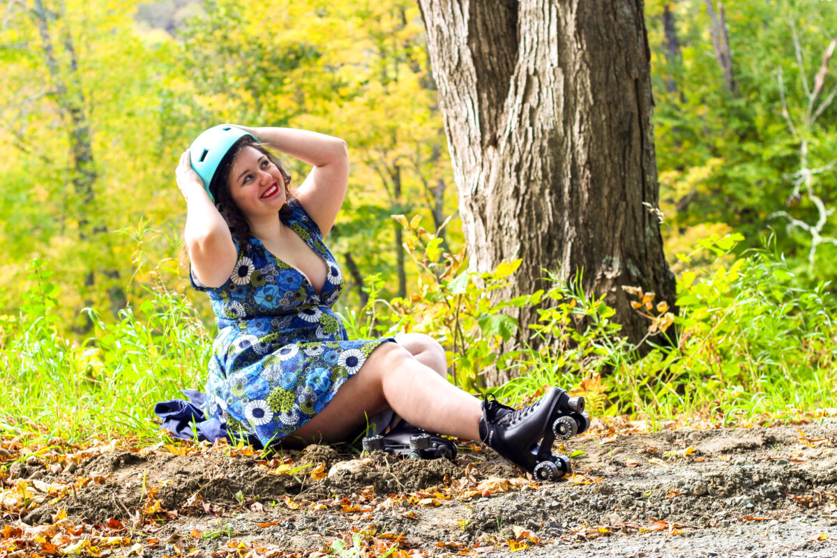 A photo of Joanna No Banana, who is the writer of this blog post, a white woman with brown, curly hair wearing a blue floral dress and black roller skates while putting on a helmet