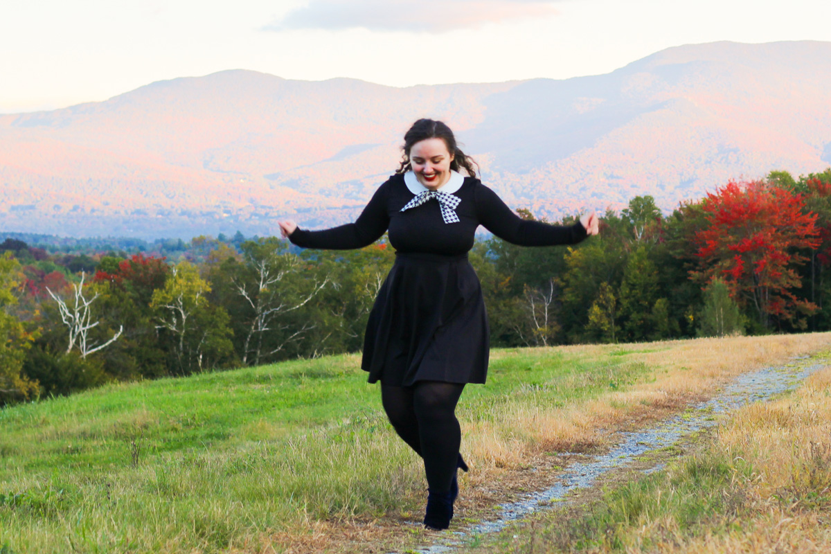A photo of Joanna No Banana, who is the writer of this blog post, a white woman with brown, curly hair wearing a dark blue dress walking outside with trees and mountains in the background