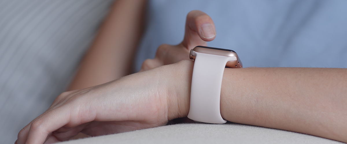 women wearing a blue shirt looking at her smart watch with her arm rested on a pillow