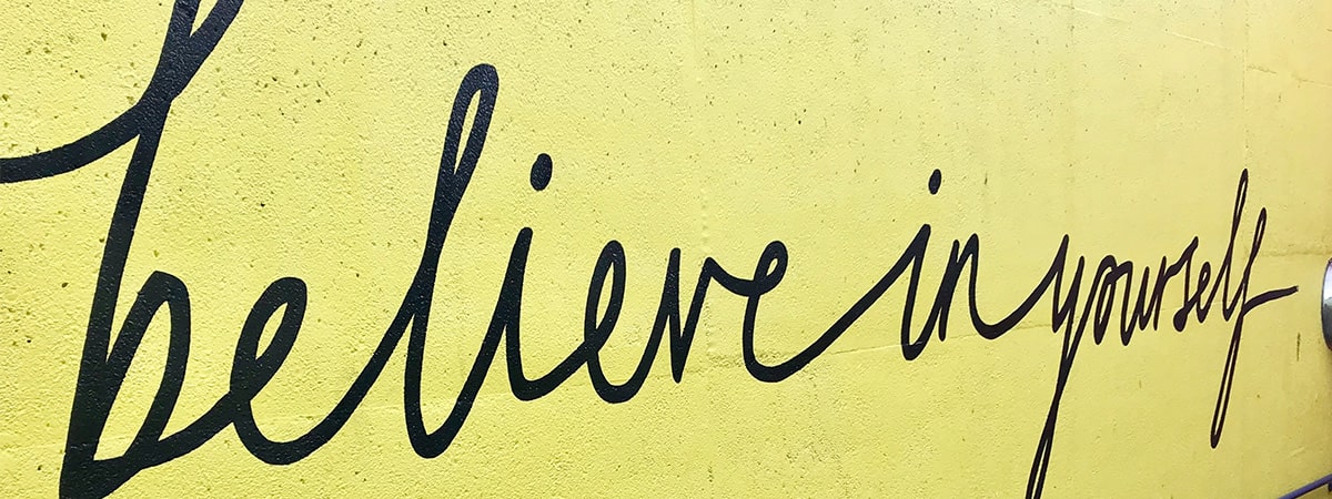Believe in yourself painted in black on a yellow exterior wall